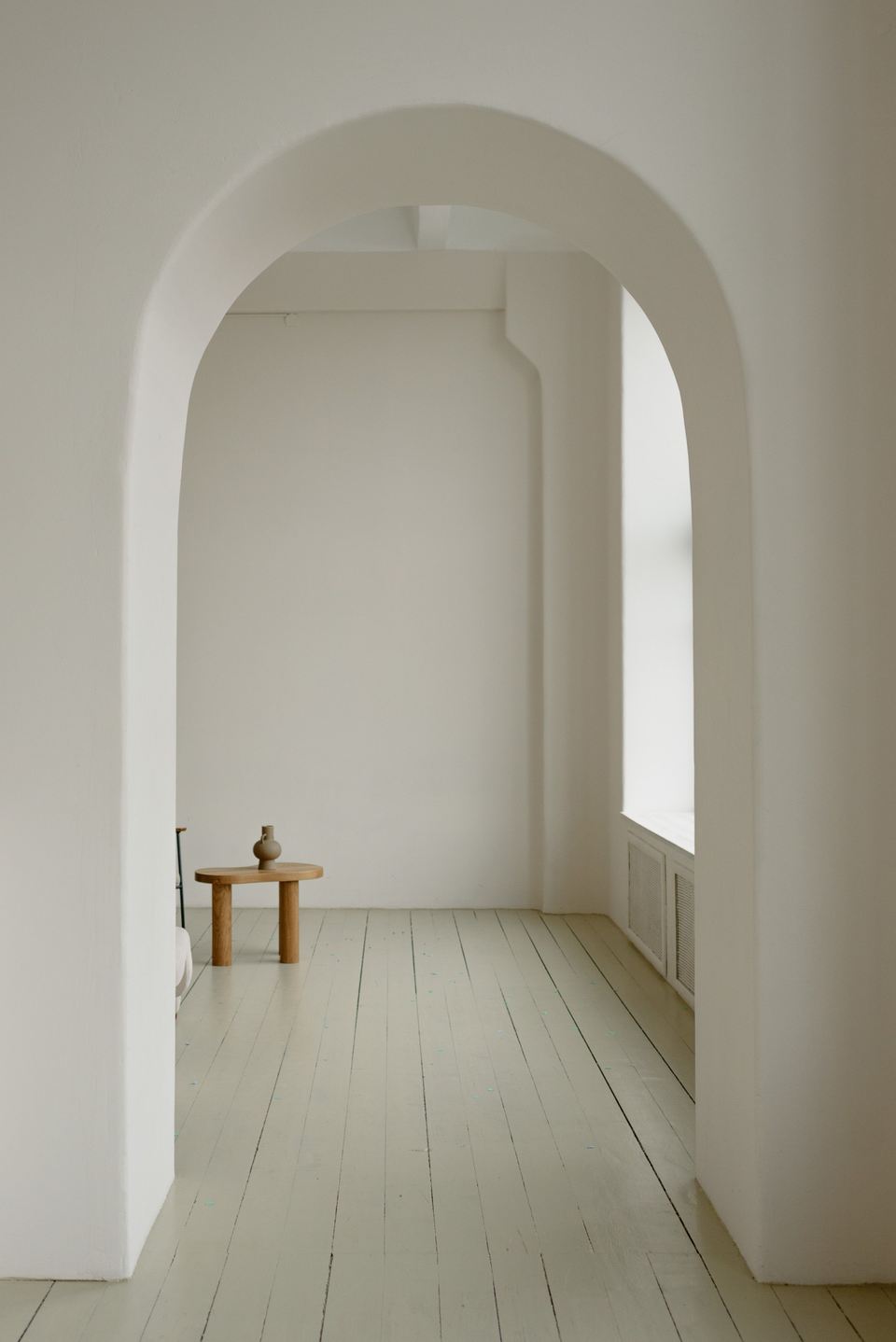 Pièce blanchie à la chaux sous une arche, parquet clair et petit tabouret