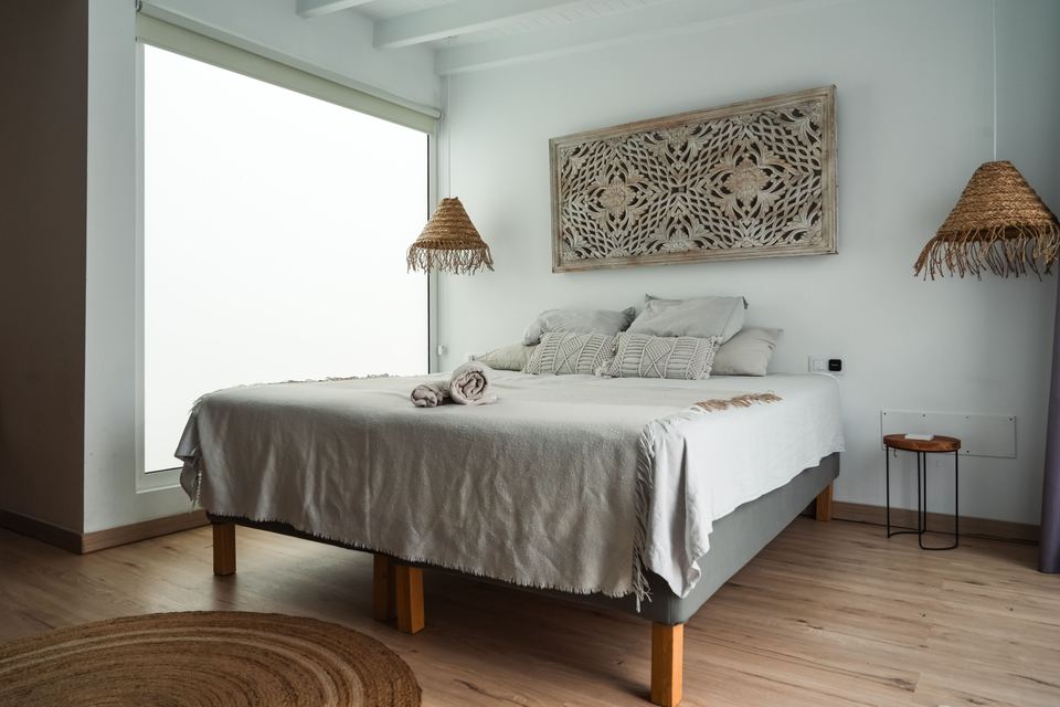 Chambre blanche, lit au jeté de lin gris, serviettes pliées et suspensions en rotin