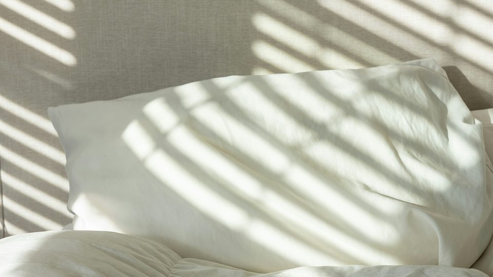 Literie blanche zébrée par l’ombre d’une persienne