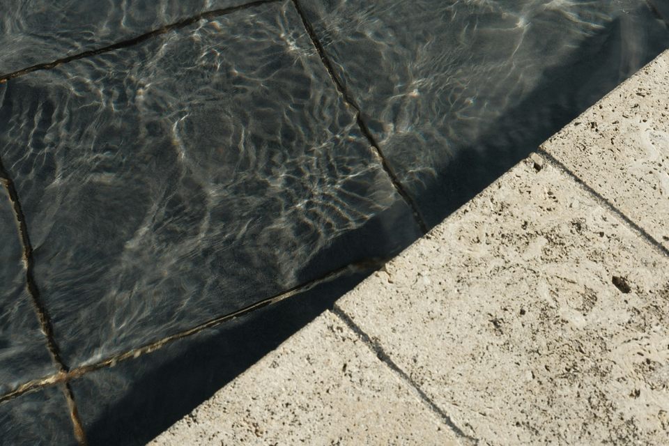 Margelle de pierre claire au bord d’une piscine, reflets sur l’eau